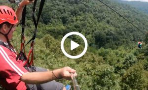person holding a camera while riding a zipline over forest