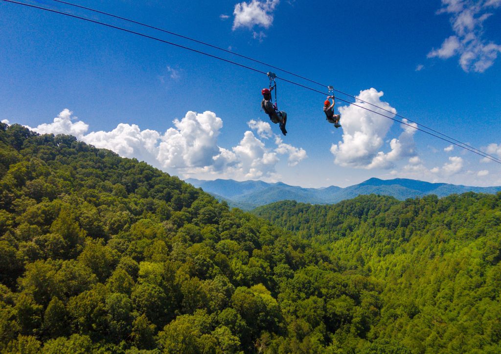 two people zip lining over forested mountains below while on mountaintop tour